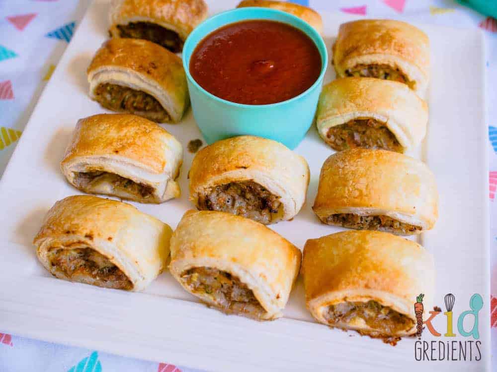 sausage rolls on a platter with a bowl of tomato sauce in the middle