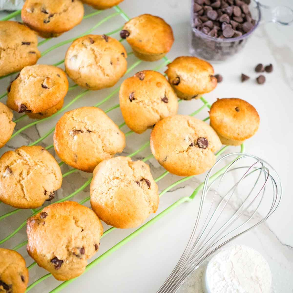 choc chip mini muffins, on a rack with a whisk and choc chips