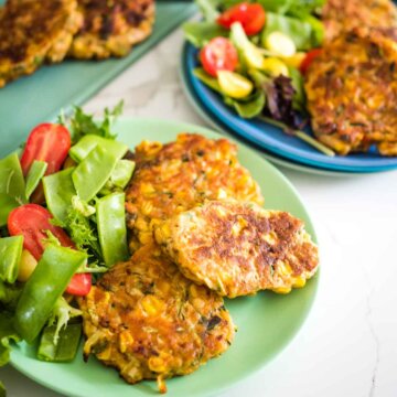 corn and zucchini fritters on a plate with a side salad