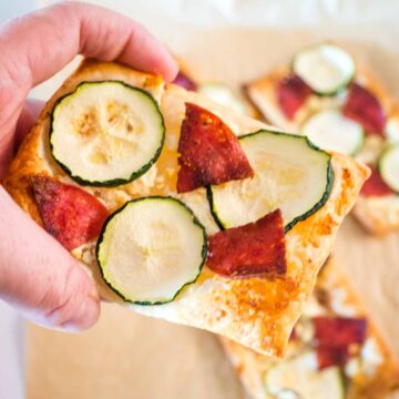 puff pastry pizza with salami and zucchini being held
