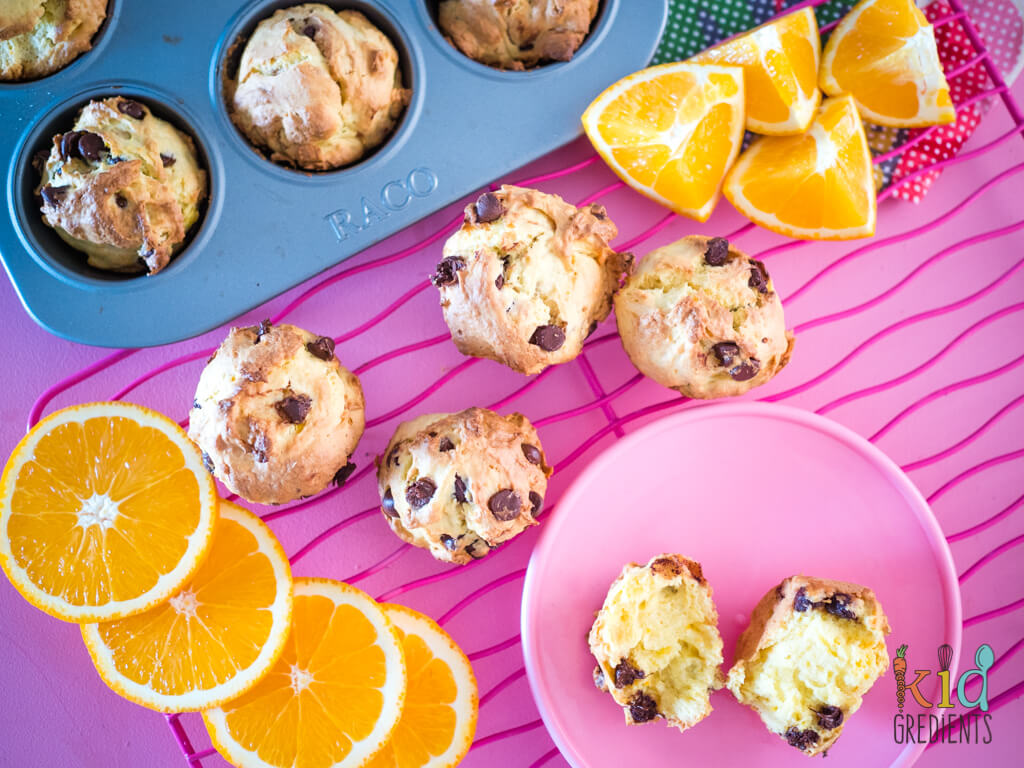 orange muffins, on a wire rack, in the muffin pan and surrounded by chopped and sliced oranges