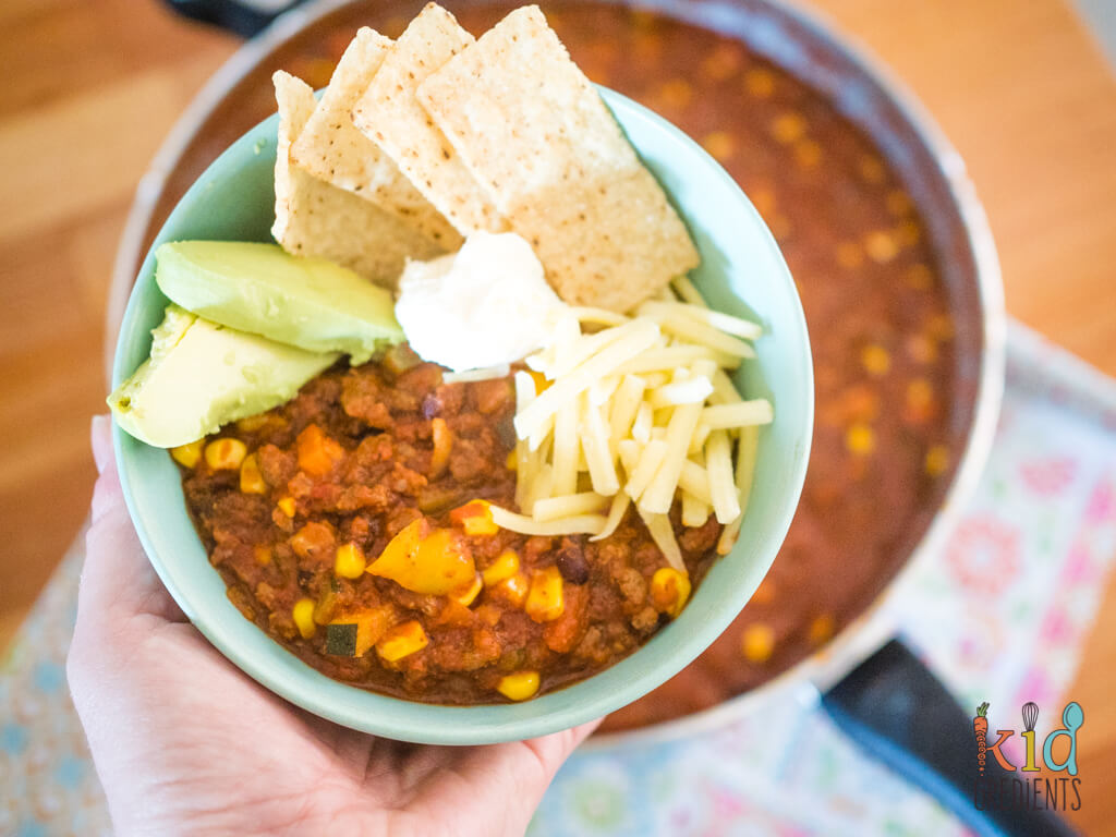 A bowl of chilli con carne with avocado, corn chips, sour cream and cheese