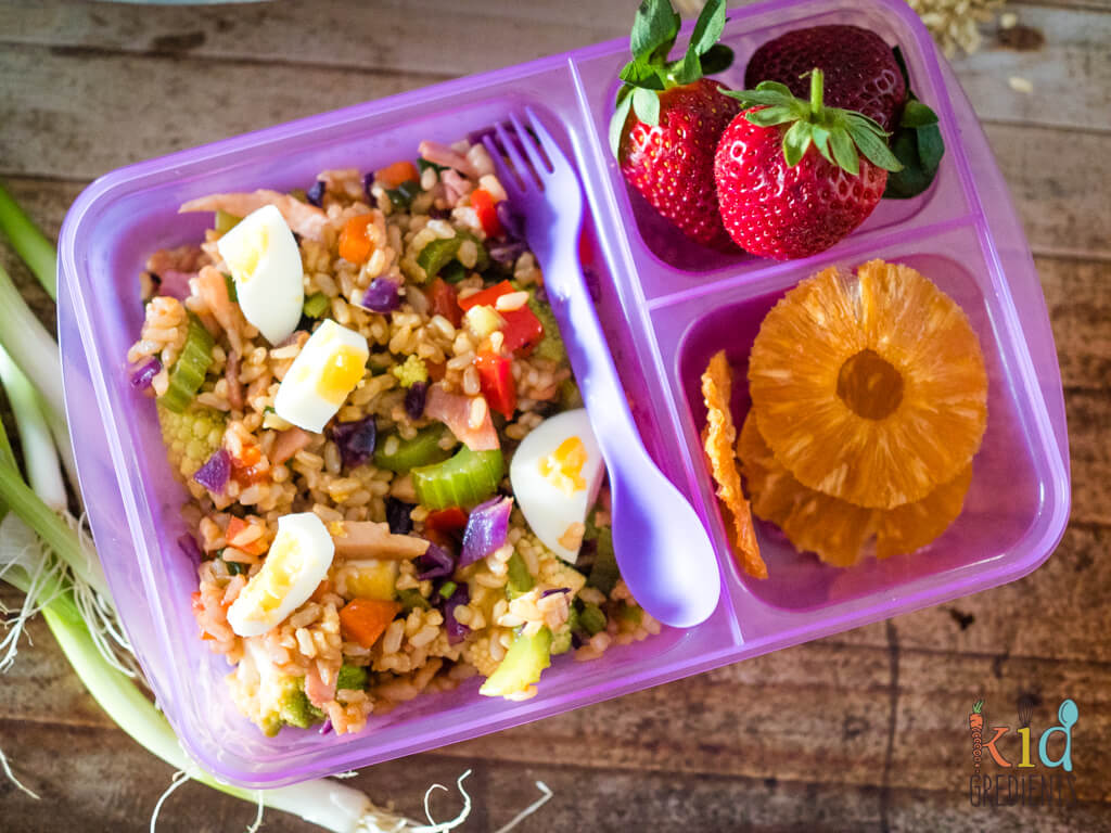 A plastic container filled with rice salad and dried pineapple and strawberries