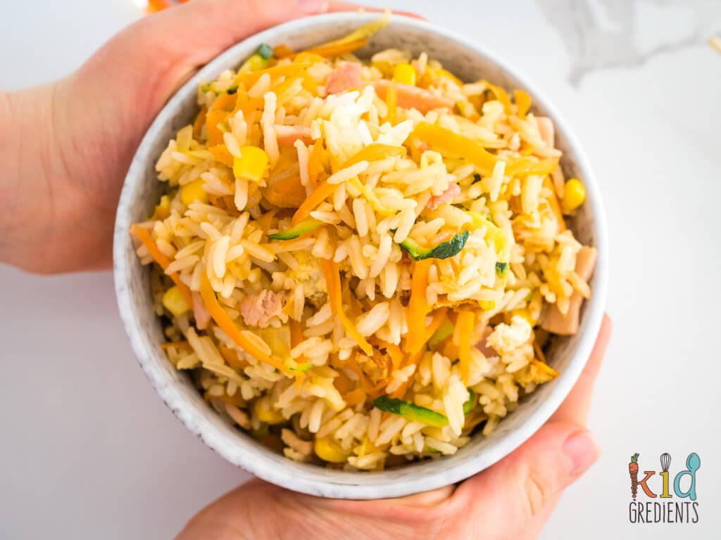 a bowl of fried rice with a child's hand around it