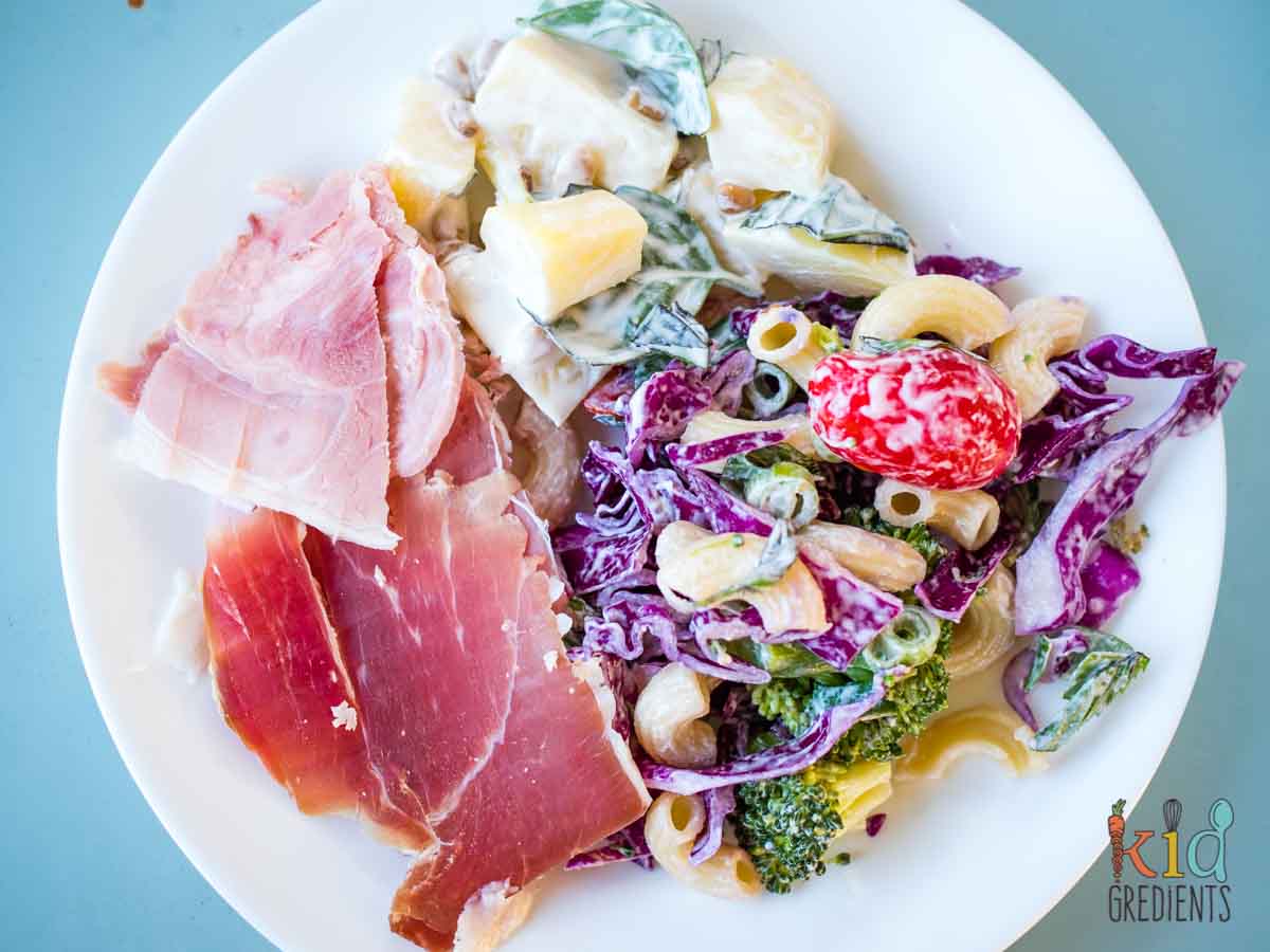 red and green festive pasta salad on a plate with ham and serrano ham and potato salad