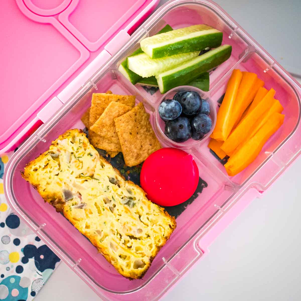easy zucchini slice in a yumbox lunchbox with veggies and crackers