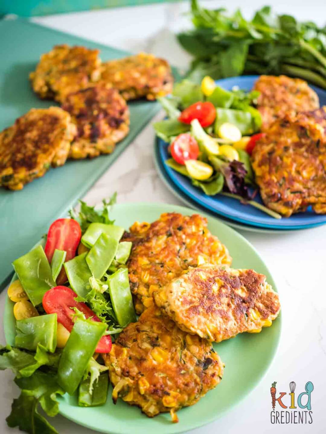 corn and zucchini fritters on plates with side salad with more fritters on a board
