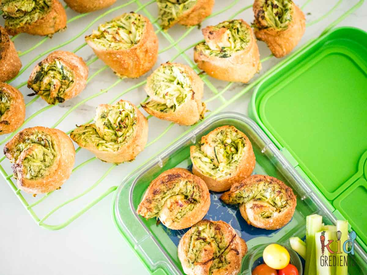spinach pinwheels in a green lunchbox and on a baking tray
