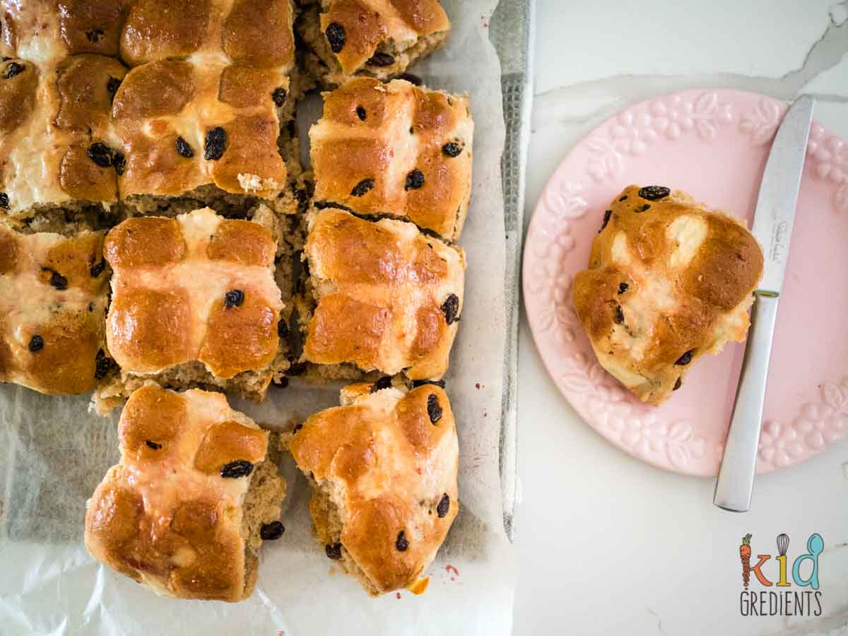 hot cross buns on baking paper and one on a pink plate