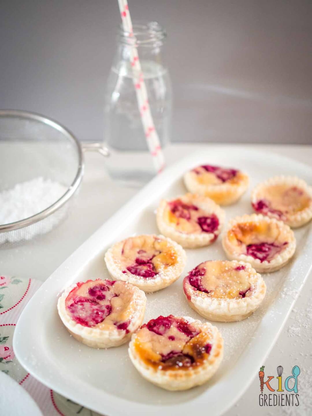 ricotta raspberry tarts on a plate with a bottle of water in the background and a sieve