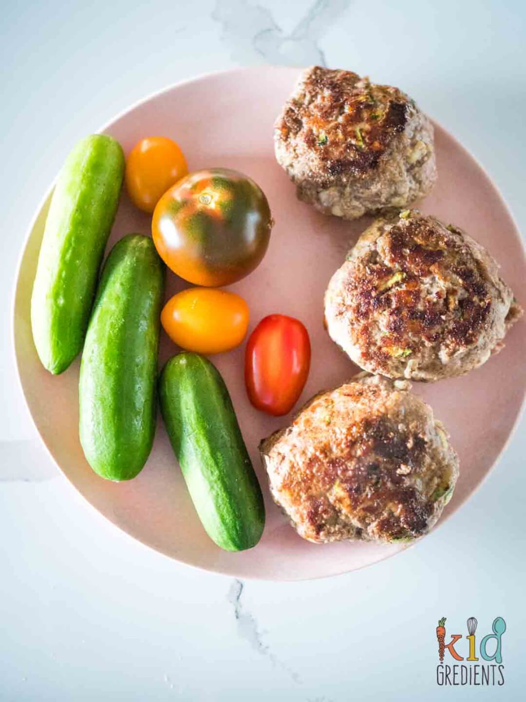 beef rissoles on a plate with qukes and cherry tomatoes