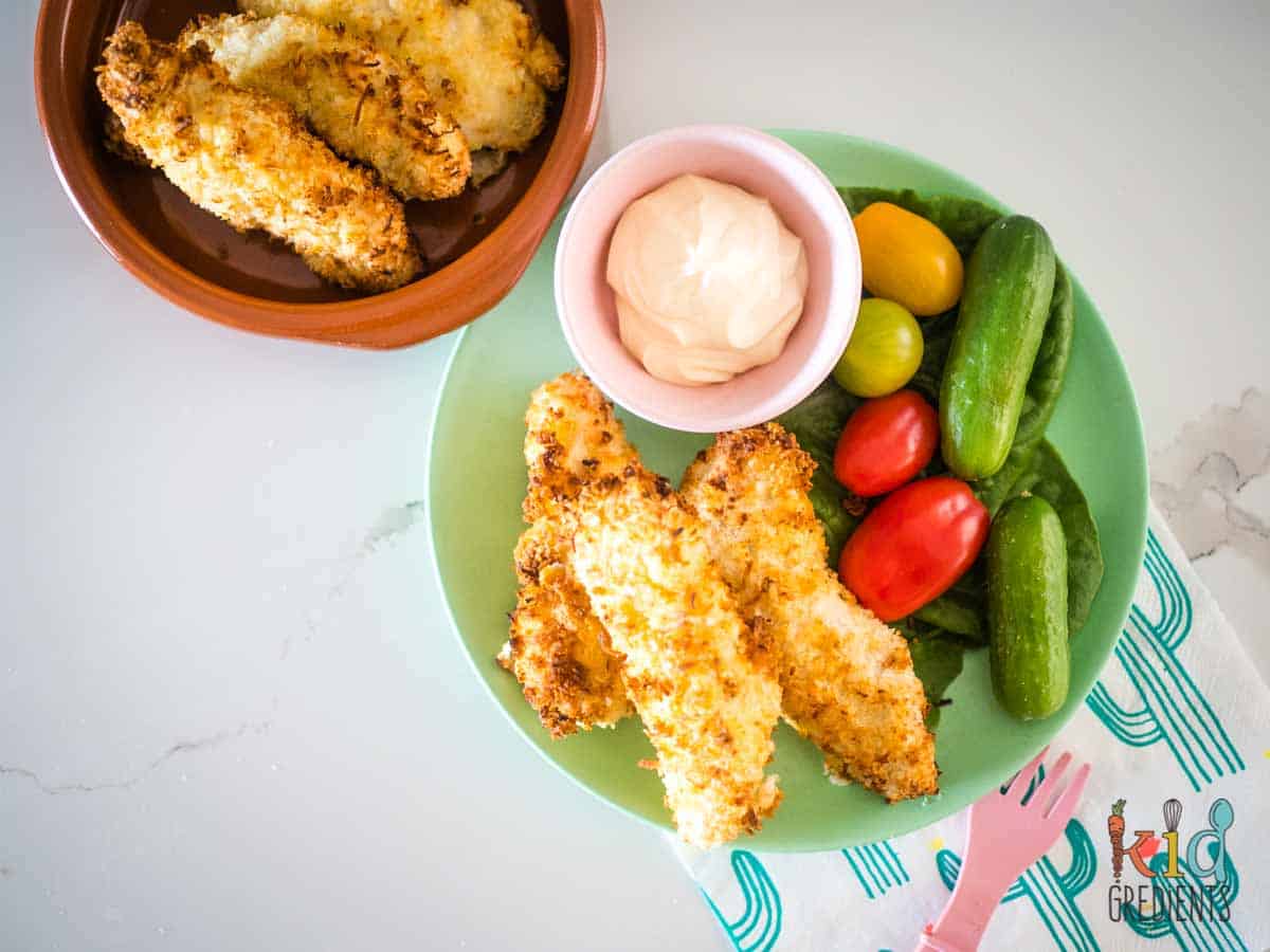 Coconut chicken tenders on a plate with tomatoes and cucumbers and mayonnaise