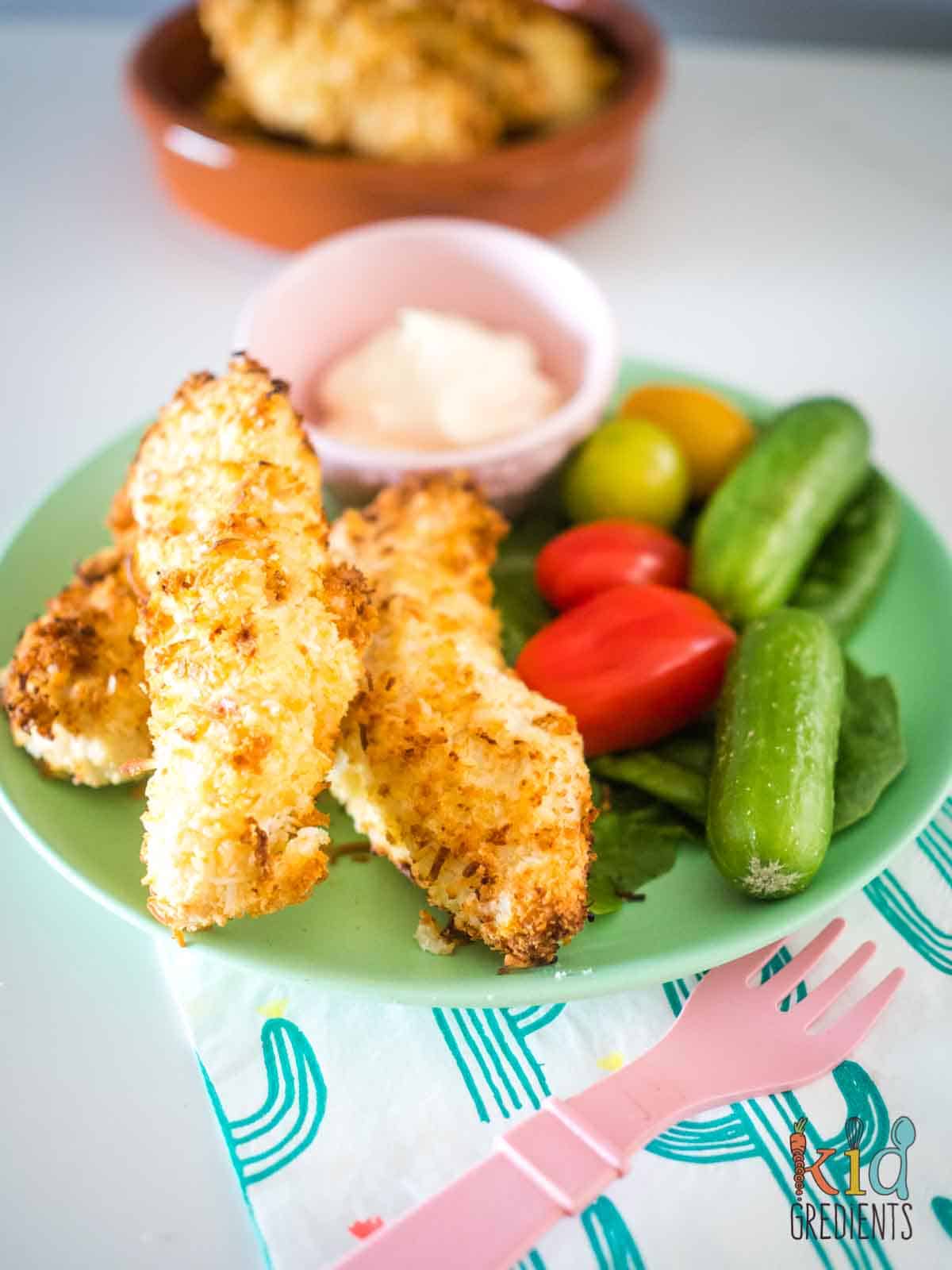 Coconut Chicken Tenders on a plate with cucumbers, cherry tomatoes and lettuce and mayonnaise as a dipping sauce