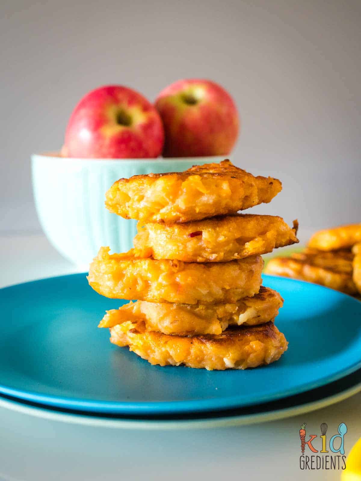Stack of Sweet Potato and Apple fritters on a plate with a bowl of apples in the background.