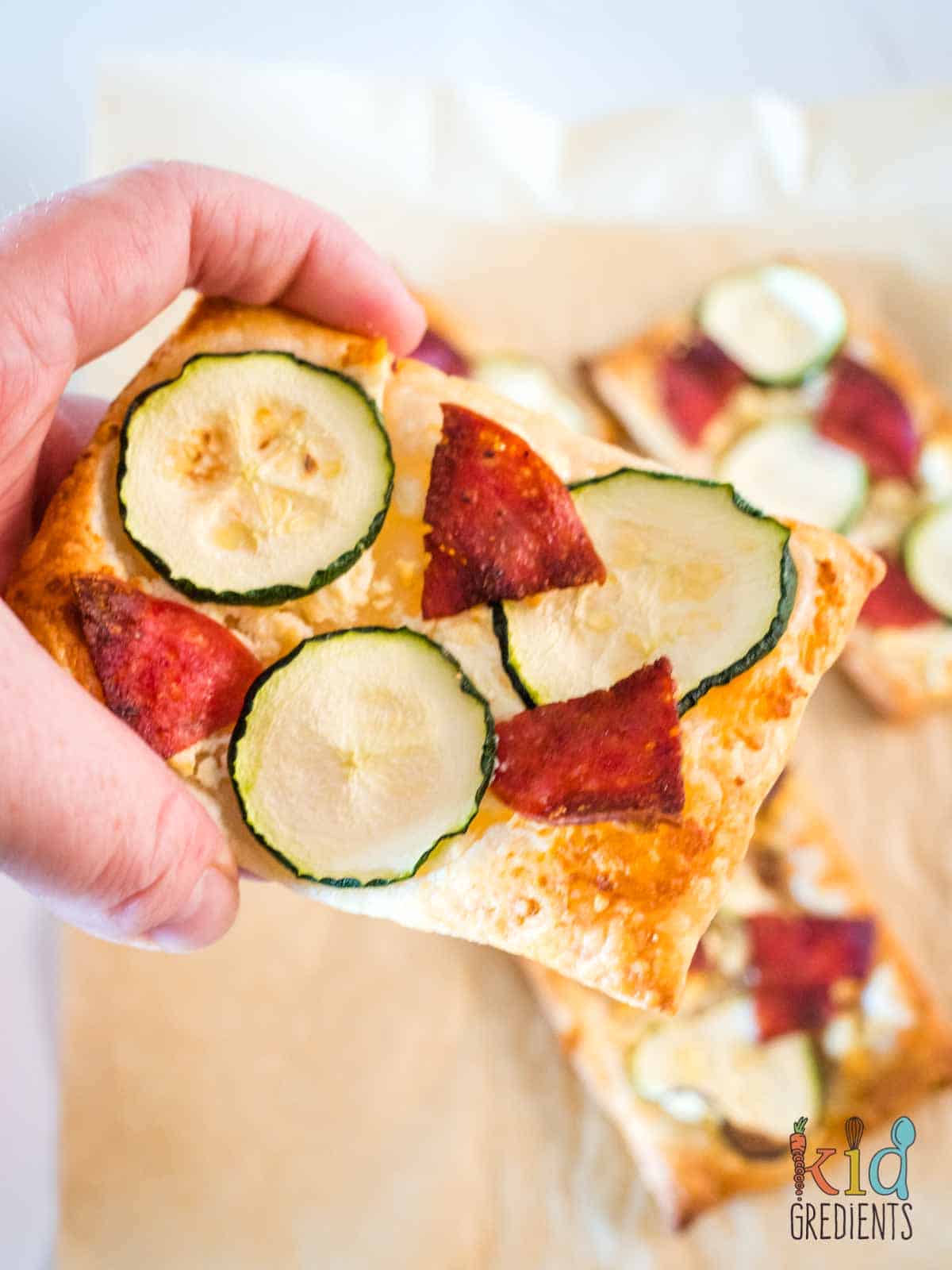 puff pastry pizzas held in a hand with salami and zucchini