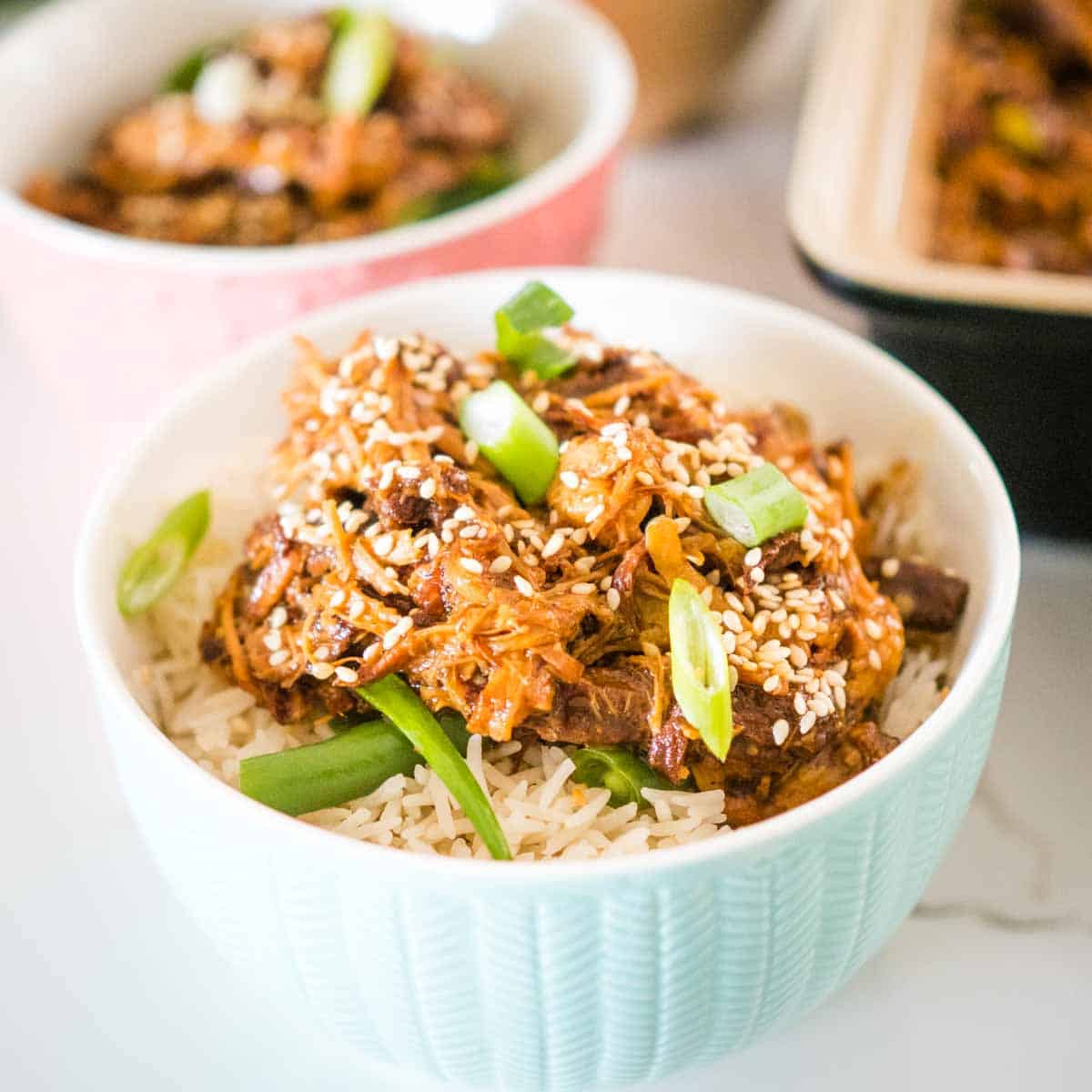 bowl of asian pulled pork topped with spring onions and sesame seeds