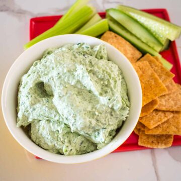 creamy spinach and fetta dip on a plate with crackers and cucumber