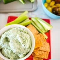 creamy spinach and fetta dip in a bowl with crackers and cucumber