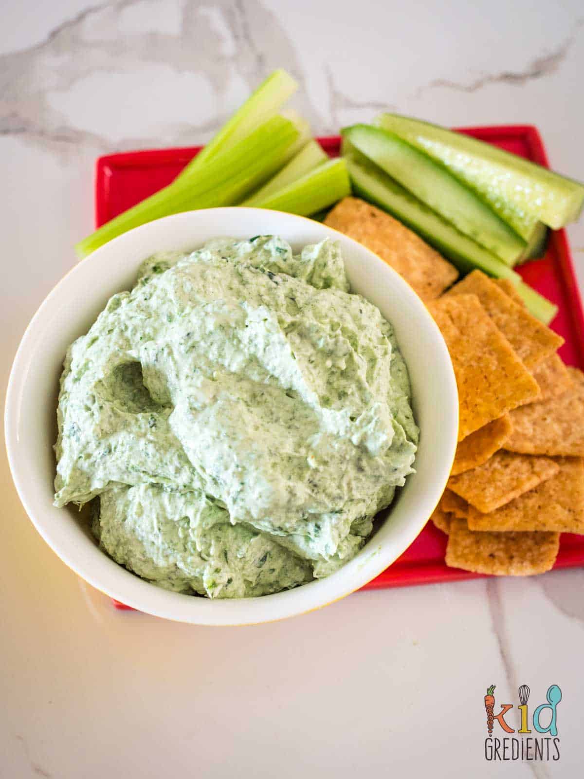 creamy fetta and spinach dip in a bowl with crackers and cucumber