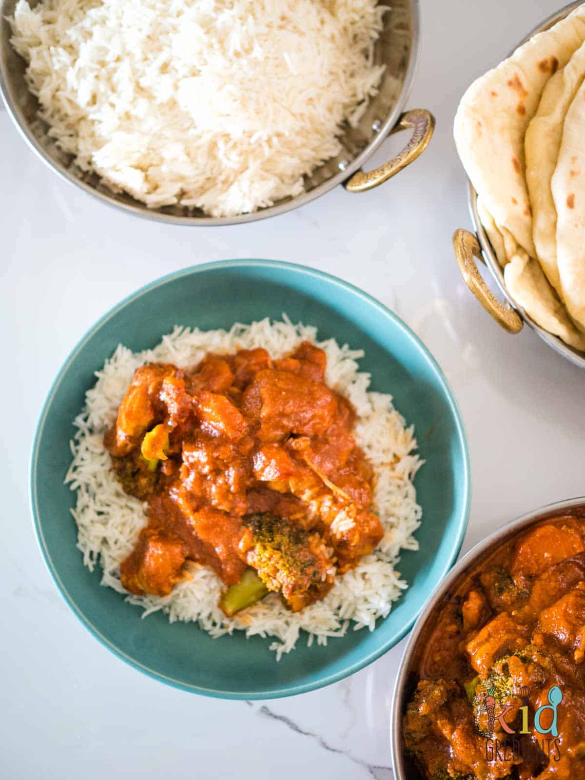 healthier butter chicken with vegetables in a bowl with rice, surrounded by rice, curry and flatbreads