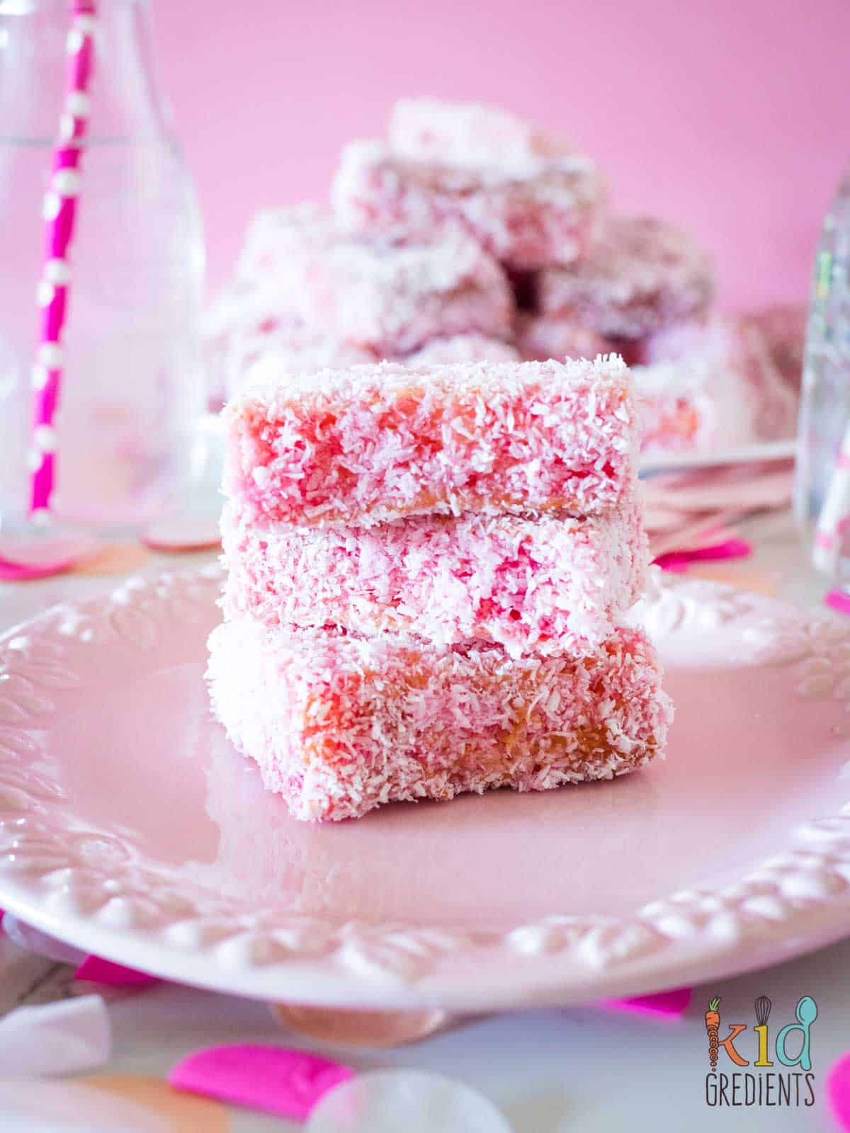 Pink lamingtons on a pink plate, with a pile of pink lamingtons behind