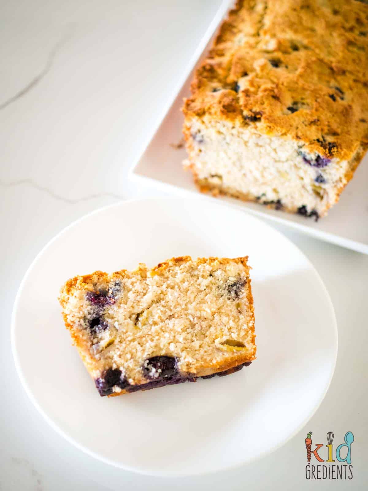 slice of blueberry banana bread on a plate with the loaf behind