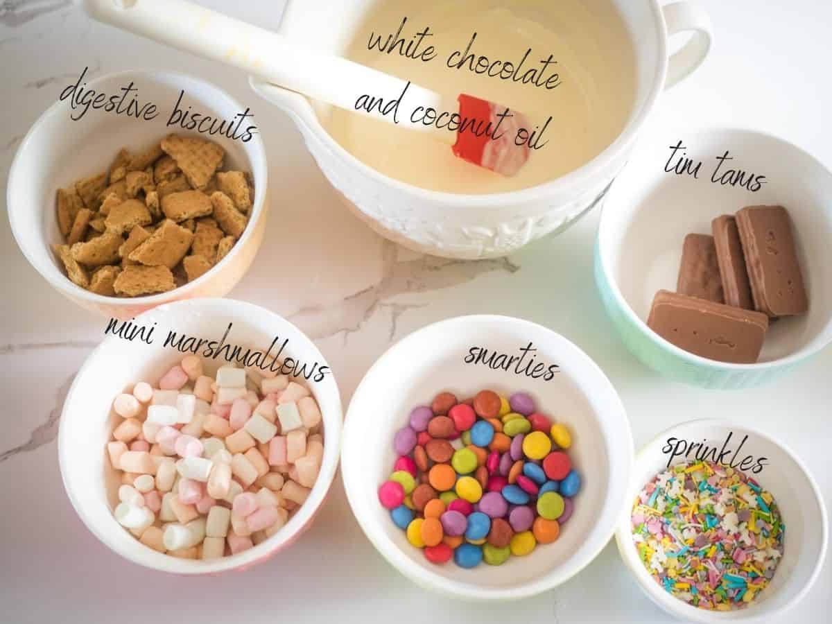 ingredients for white chocolate rocky road: white chocolate, coconut oil, smarties, digestives, mini marshmallows, tim tams and sprinkles.