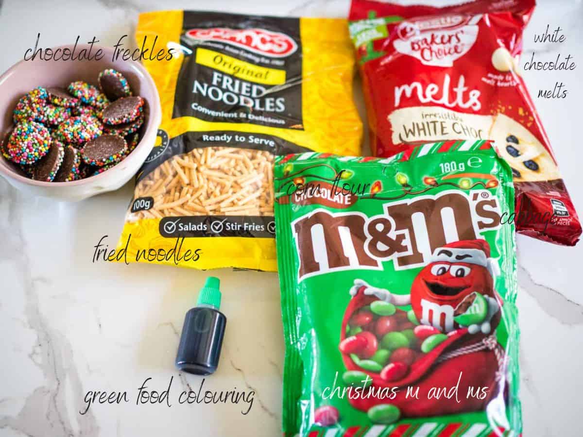ingredients for chocolate christmas wreaths: white chocolate melts, m and ms, fried noodles, chocolate freckles, green food colouring.